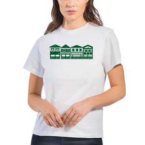 May include: White t-shirt with a green graphic depicting a row of houses. The houses have different designs, including windows and doors. The shirt is made of a soft material and has a crew neck.