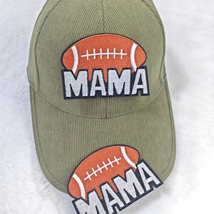 May include: Olive green corduroy baseball cap with an embroidered football and the word "MAMA" in white block letters. The football is orange with white stitching. The cap is a classic six-panel design.