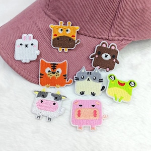 May include: A collection of embroidered animal patches, including a rabbit, giraffe, bear, tiger, cat, frog, cow, and pig. The patches are colorful and have a cartoon-like design. The patches are on a pink baseball cap.
