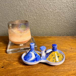 May include: A ceramic salt and pepper set with blue and yellow designs, and a glass cup with iridescent colors. The salt and pepper set has a blue and white swirl design on one side and a yellow and green star design on the other.