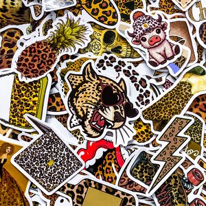 May include: A collection of colorful stickers with various designs. The stickers feature a pineapple, a leopard with heart-shaped sunglasses, a cow wearing a hat, and leopard print patterns. The stickers are white-bordered and have a glossy finish.