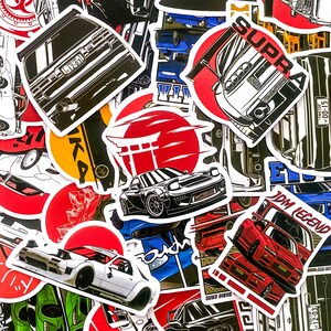 May include: A collection of car-themed stickers featuring various Japanese Domestic Market (JDM) car designs. The stickers showcase detailed illustrations of vehicles, including the word "SUPRA" and Japanese text, with red and black color schemes.
