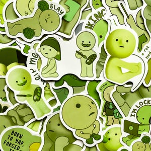 Op de afbeelding: Een verzameling groene stickers met cartoonfiguren in verschillende poses. Sommige stickers hebben tekst zoals "SLAY", "BORN" en "I'M LOCK". De stickers zijn in groentinten, met witte randen.