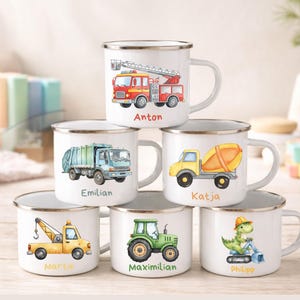 May include: Six white enamel mugs with silver rims, each featuring a unique watercolour illustration of a construction vehicle or dinosaur and a personalised name: Anton, Emilian, Katja, Martin, Maximilian, and Philipp printed below the graphic.
