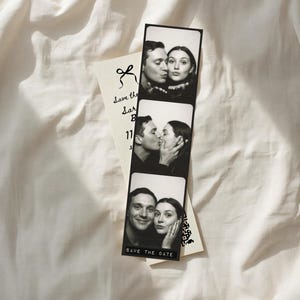 May include: A monochrome photo strip featuring three images of a couple, kissing and smiling. A cream card with "Save the Date" and a bow graphic is next to the strip. The background is a white, textured fabric.