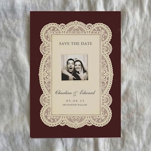 May include: A maroon Save the Date card with a cream-colored lace border. The card features a black and white photo of a couple and the text "Save the Date," along with names and a date.