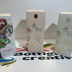 Könnte beinhalten: Drei Champagner-Kartons mit floralen Designs. Die Kartons sind rechteckig und tragen die Marke Perrier-Jouët. Eine Schachtel hat ein Schmetterlings- und Blumendesign, eine andere rosa Blumen und die dritte ein Blumendesign mit goldenen Akzenten.