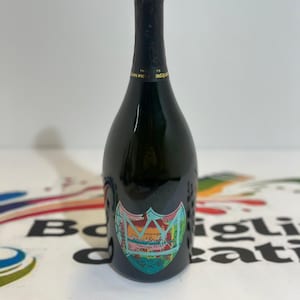 Pu&ograve; includere: Una bottiglia di champagne verde scuro con un'etichetta colorata. L'etichetta presenta un disegno a stemma con le parole "Dom P&eacute;rignon Vintage 2010". La bottiglia ha una parte superiore in lamina nera ed &egrave; posta su uno sfondo bianco.
