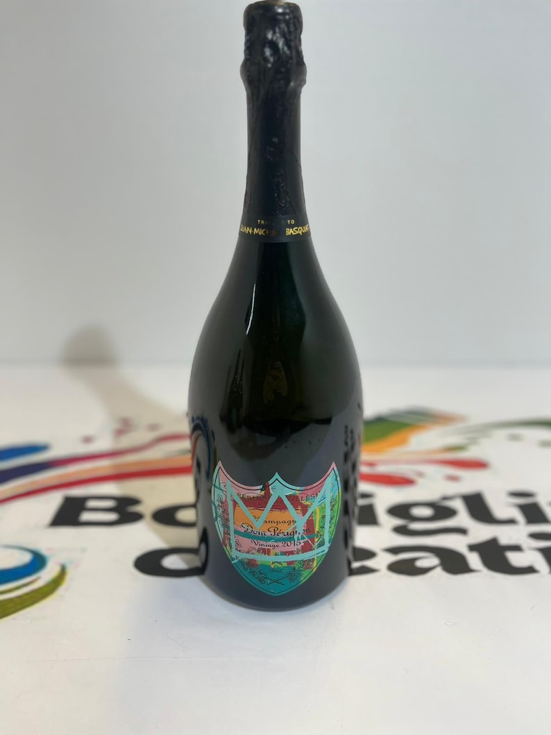 Pu&ograve; includere: Una bottiglia di champagne verde scuro con un'etichetta colorata. L'etichetta presenta un disegno a stemma con le parole "Dom P&eacute;rignon Vintage 2010". La bottiglia ha una parte superiore in lamina nera ed &egrave; posta su uno sfondo bianco.