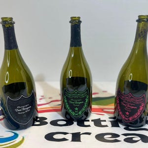 Może przedstawiać: Trzy puste butelki po szampanie z zielonego szkła z etykietami. Lewa butelka ma czarną etykietę z napisem Dom P&eacute;rignon Vintage 2015. Środkowa butelka ma zieloną etykietę z napisem Dom P&eacute;rignon Vintage. Prawa butelka ma r&oacute;żową etykietę z napisem Dom P&eacute;rignon Ros&eacute; Vintage.