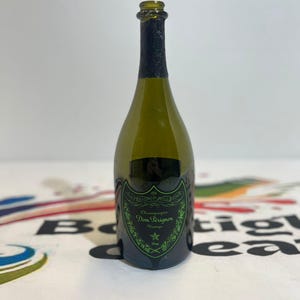 Może przedstawiać: Pusta butelka szampana Dom P&eacute;rignon z zielonego szkła z czarną folią na szyjce i czarną etykietą z zielonym napisem Dom P&eacute;rignon, Champagne, Vintage i Mill&eacute;sime, ozdobioną zieloną ramką oraz ikoną gwiazdy.