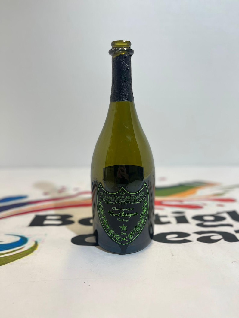 Może przedstawiać: Pusta butelka szampana Dom P&eacute;rignon z zielonego szkła z czarną folią na szyjce i czarną etykietą z zielonym napisem Dom P&eacute;rignon, Champagne, Vintage i Mill&eacute;sime, ozdobioną zieloną ramką oraz ikoną gwiazdy.
