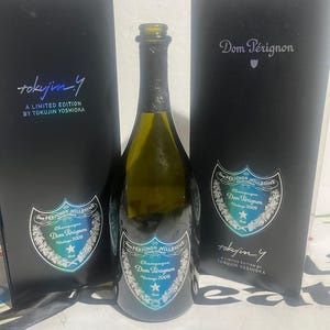 Könnte beinhalten: Eine dunkelgrüne Glasflasche Dom Pérignon Vintage 2009 Champagner, platziert zwischen zwei schwarzen rechteckigen Geschenkboxen. Jede Box und das Flaschenetikett tragen den Text Dom Pérignon, Vintage 2009 und Tokujin Yoshioka Limited Edition.