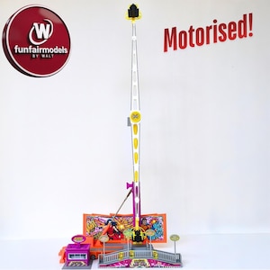 May include: A model fairground ride featuring a tall, yellow and white tower, a purple support structure, and an orange base. The model includes a ticket booth and a bridge. The words "Motorised!" are in red.