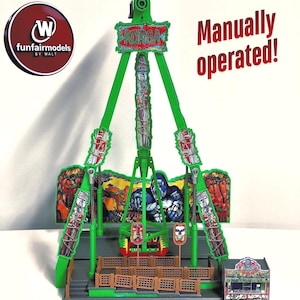 May include: A green model amusement ride labeled KONGA featuring a central tower, a swinging arm, and a backdrop illustration of a gorilla. The model includes a small ticket booth, brown fencing, and the text Manually operated! printed on the side.