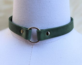 Könnte beinhalten: Ein dunkelgrünes Lederhalsband mit einem silbernen Ringakzent. Das Halsband ist verstellbar und hat ein schlichtes Design.