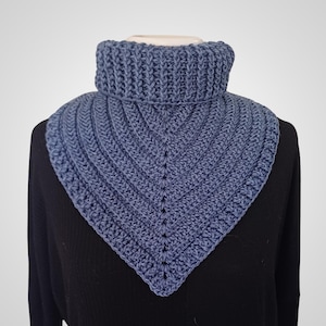 Puede incluir: Un calentador de cuello azul tejido a ganchillo. El calentador de cuello tiene un cuello alto acanalado y una forma triangular. El cuello es de color azul liso y parece estar hecho de un hilo suave. El cuello se muestra en un maniquí.