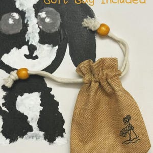 Pu&ograve; includere: Un piccolo sacchetto con coulisse beige con ricamo floreale, accompagnato da un cordoncino color crema e perline di legno. Le parole "Soft Bag Included" sono scritte in arancione. Un'illustrazione di cane in bianco e nero &egrave; sullo sfondo.