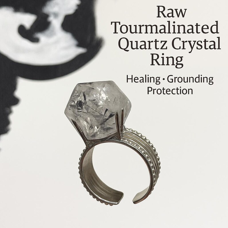 Pu&ograve; includere: Un anello di cristallo di quarzo tormalinato grezzo. L'anello presenta un grande cristallo di quarzo trasparente sfaccettato con inclusioni nere, incastonato in una fascia regolabile color argento. Il testo sull'immagine recita "Raw Tourmalinated Quartz Crystal Ring" e "Healing, Grounding, Protection."