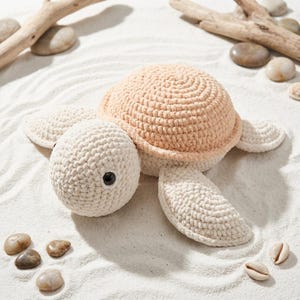 May include: A crocheted sea turtle toy featuring a soft cream-coloured head and flippers paired with a textured, rounded shell in a light peach hue. The turtle has two dark, round plastic eyes set into the cream-coloured yarn of its head.