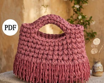 May include: A dusty rose-colored handbag with a braided handle and beaded fringe. The bag is made of a thick, textured material and has a rounded shape. The word "PDF" is in a white circle on the bag.