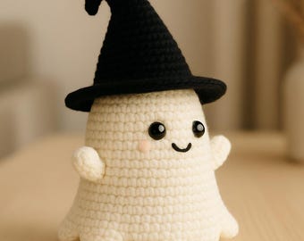 Puede incluir: Un fantasma tejido a ganchillo con un sombrero de bruja negro. El fantasma es de color blanco roto con una cara sonriente, mejillas rosadas y brazos pequeños. El sombrero tiene una parte superior curva y un ala ancha. Artículo hecho a mano.