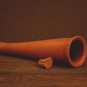 以下が含まれることがあります： テラコッタ粘土製のワインクーラー。開口部はフレア状で、別のストッパーが付いています。ワインクーラーは円筒形で、木製の表面に置かれています。背景は単色の茶色です。