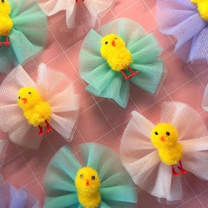 May include: A selection of decorative bows, each featuring a yellow chick. The bows are crafted from tulle in pastel shades like blue, green, and pink. The chicks have red feet and black eyes.