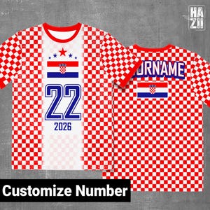 May include: A short-sleeve t-shirt featuring a red and white checkered pattern. The front displays the Croatian flag, the number 22, and the year 2026. The back shows the text YOURNAME above the Croatian flag. The design includes a red crew neck.
