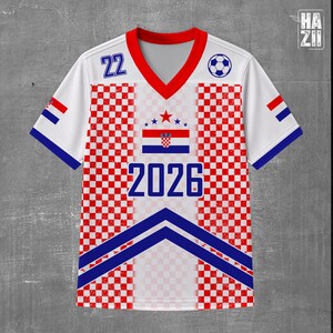 May include: A white V-neck jersey featuring a red and white checkered pattern on the sides, blue chevron stripes at the bottom, the number 22, the year 2026, a soccer ball icon, and a central graphic of the Croatian flag with stars above it.