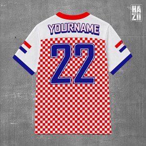 May include: A white short-sleeved jersey featuring a red and white checkered pattern on the lower half. The back displays the text YOURNAME in blue with a white outline above the large blue number 22. The sleeves have red and blue accents.