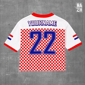 May include: A white short-sleeved jersey featuring a red and white checkered pattern on the lower half. The back displays the text YOURNAME in blue and the number 22 in large blue digits. The sleeves have red trim and a small Croatian flag emblem.