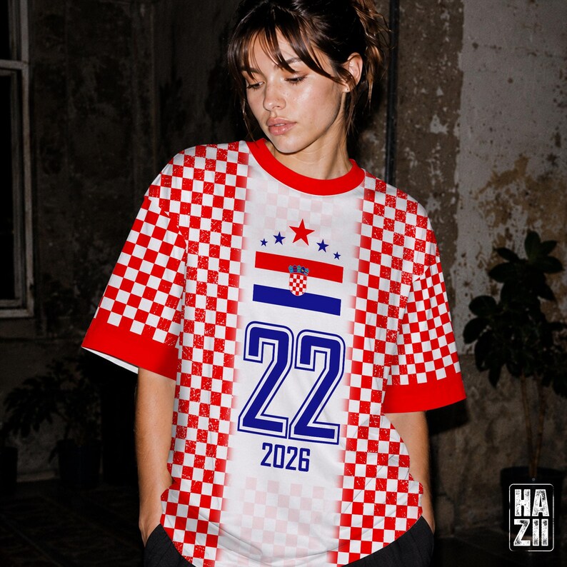 May include: A short-sleeved t-shirt featuring a red and white checkered pattern on the sides and sleeves. The center panel is white with the Croatian flag, a red star, the number 22 in blue, and the text 2026 printed in blue below the number.