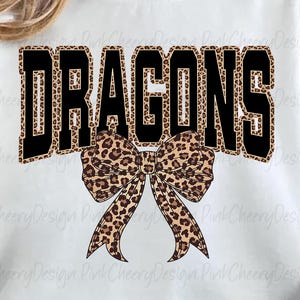 May include: White sweatshirt with the word "DRAGONS" in large black block letters with a leopard print fill. A leopard print bow is centered below the word. The sweatshirt is a casual style.