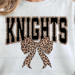 May include: White sweatshirt with the word "KNIGHTS" in black block letters with a leopard print fill. A leopard print bow is centered below the word. The sweatshirt is a casual style.