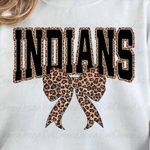 Könnte beinhalten: Weißes Sweatshirt mit dem Wort "INDIANS" in schwarzen Blockbuchstaben mit Leopardenmuster. Eine Leopardenmuster-Schleife befindet sich darunter. Das Sweatshirt hat einen Rundhalsausschnitt.