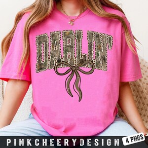 May include: A bright pink t-shirt with the word "DARLIN" in a camouflage and leopard print design. A brown bow with white accents is below the word. The text "PINKCHEERYDESIGN 4 PNGS" is at the bottom.