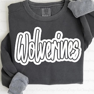 Op de afbeelding: Een donkergrijs sweatshirt met het woord "Wolverines" in grote witte, omrande letters op de voorkant. De sweatshirt heeft een ronde hals en lange mouwen met grijze, fuzzy manchetten. Het label luidt "Comfort Colors".