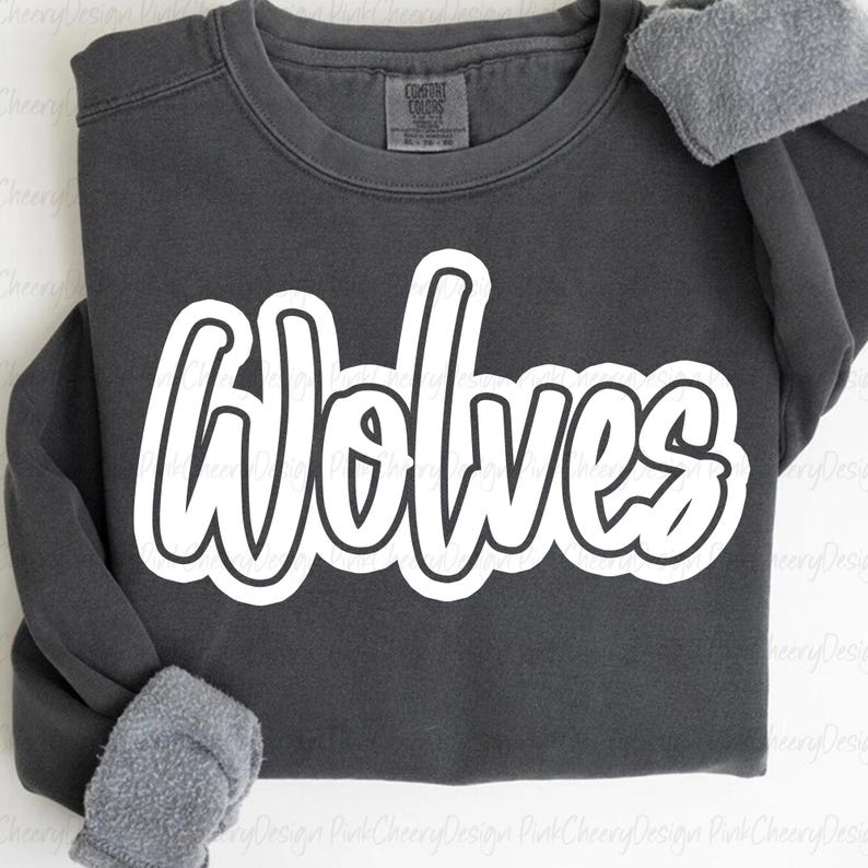 May include: A dark gray sweatshirt with the word "Wolves" in large, white, cursive lettering. The sweatshirt has a crew neck and long sleeves with gray, fuzzy cuffs. The Comfort Colors tag is visible.