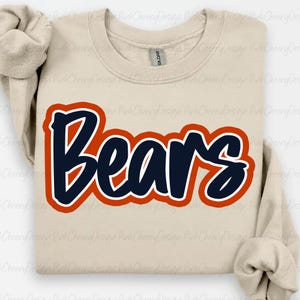 May include: A beige sweatshirt with the word "Bears" in navy blue, outlined in orange and white. The sweatshirt has a crew neck and long sleeves. The text is in a bold, stylized font.