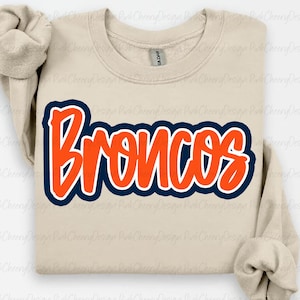 May include: A beige sweatshirt with the word "Broncos" in orange, outlined in navy blue. The text has a bold, playful font. The sweatshirt is a Gildan brand.