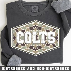 Puede incluir: Una sudadera de cuello redondo gris carbón con un gráfico hexagonal central. El gráfico contiene un patrón de camuflaje en tonos verde, marrón y bronceado, con la palabra COLTS impresa en letras grandes, blancas y desgastadas.