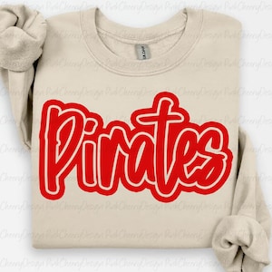 Op de afbeelding: Een beige crewneck sweatshirt met het woord "Pirates" in grote, rode, omrande letters op de voorkant. De sweatshirt heeft lange mouwen en een geribbelde halslijn. Het Gildan-merklabel is zichtbaar.
