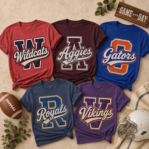May include: Five short-sleeved t-shirts in red, maroon, blue, dark blue, and purple, each featuring a large block letter and a team name in a script font. A brown football and a white football helmet are positioned near the shirts.