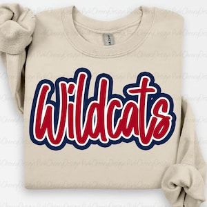 Könnte beinhalten: Beiges Sweatshirt mit dem Wort "Wildcats" in Rot, umrandet von Weiß und Marineblau. Das Sweatshirt ist von der Marke Gildan und hat lange Ärmel. Der Text ist in einer fetten, kursiven Schrift.