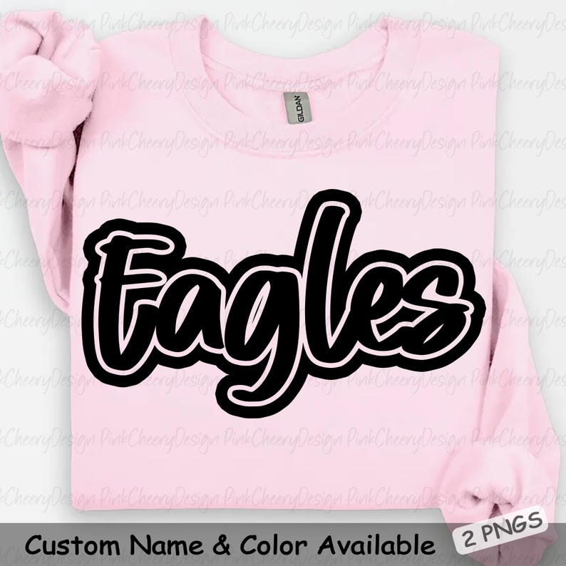May include: A light pink sweatshirt with the word "Eagles" in large, black, cursive lettering outlined in white. The text "Custom Name & Color Available" is at the bottom. The sweatshirt is folded, with the sleeves visible.