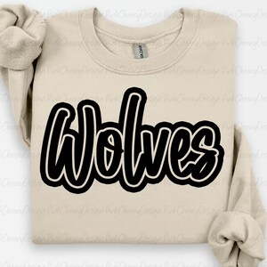 May include: A beige sweatshirt with the word "Wolves" in large, black, cursive lettering. The sweatshirt has a crew neck and long sleeves. The Gildan brand tag is visible on the neckline.