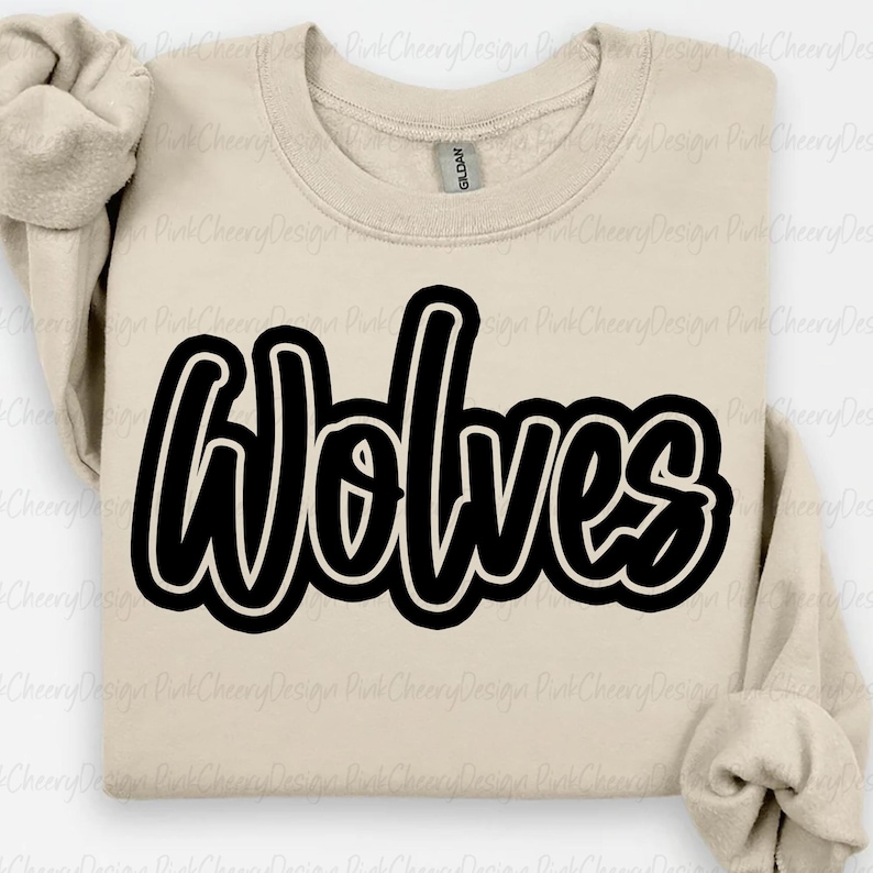 May include: A beige sweatshirt with the word "Wolves" in large, black, cursive lettering. The sweatshirt has a crew neck and long sleeves. The Gildan brand tag is visible on the neckline.