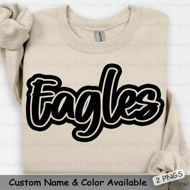 May include: A beige crewneck sweatshirt with the word "Eagles" in large, black, outlined lettering across the front. The text "Custom Name & Color Available" is at the bottom. The sleeves are folded.