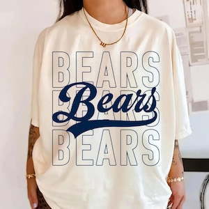 May include: Cream-colored t-shirt with the word "BEARS" in a navy blue and white design. The word "BEARS" is repeated three times, with the middle word in a cursive font. The shirt has short sleeves.